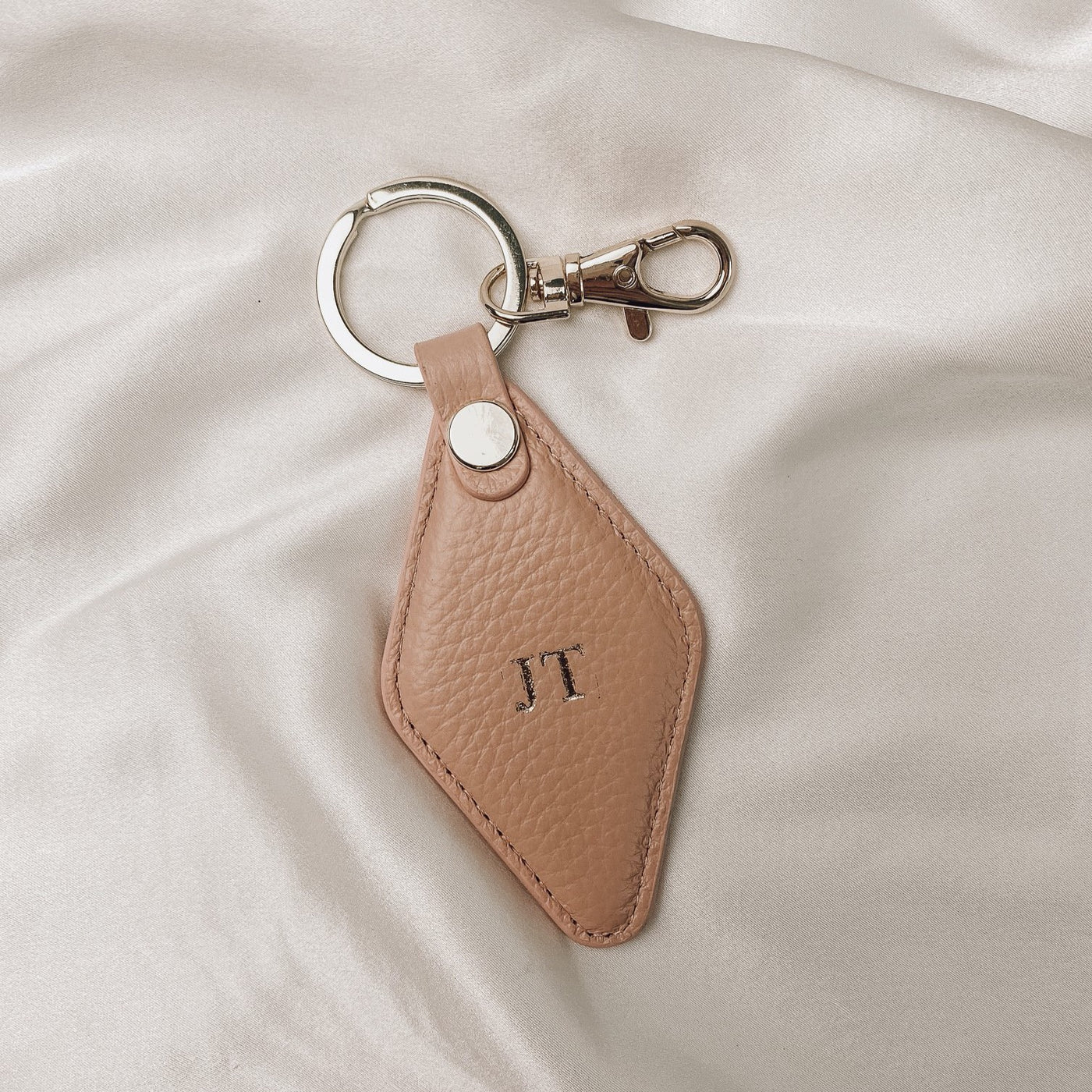 blush diamond keyring with gold hardware  on a silk backdrop. the keyring is embossed with the initials JT
