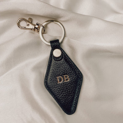 black diamond keyring with gold hardware  on a silk backdrop. the keyring is embossed with the initials DB